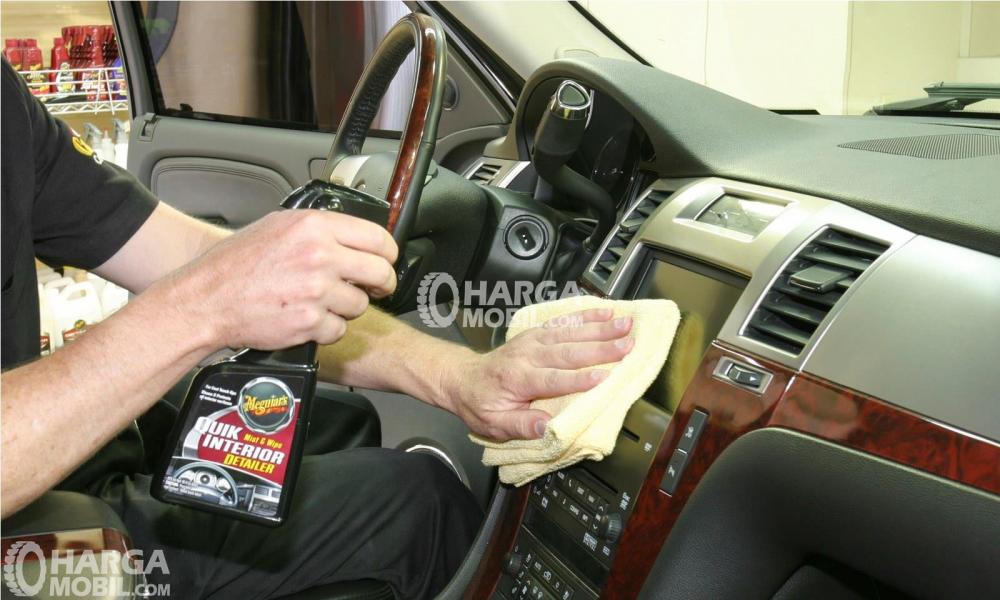 gambar seorang pria berbaju hitam sedang membersihkan dashboard dalam mobilnya dengan handuk tangan 
