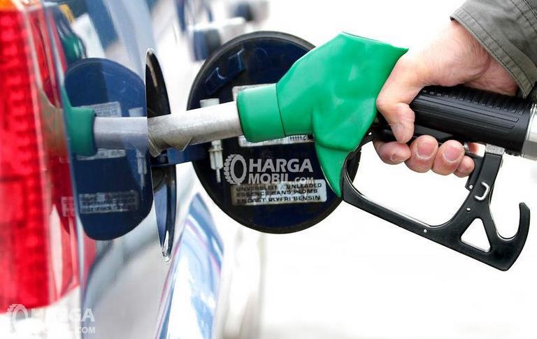 gambar ini menunjukkan sebuah tangan memegang alat pengisi bahan bakar diarahkan ke lubang tangki Mobil
