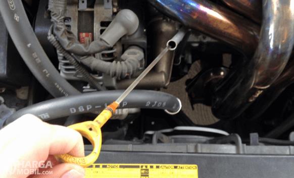 Gambar ini menunjukkan sebuah tangan menarik stik oli pada mesin mobil