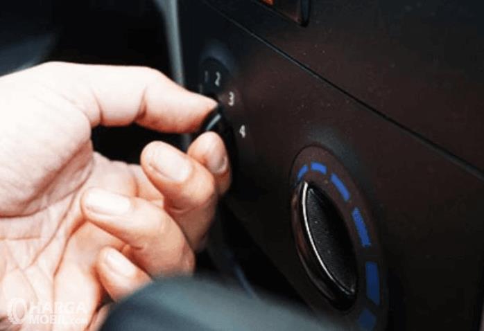 Gambar ini menunjukkan sebuah tangan memegang knop pengatur AC Mobil