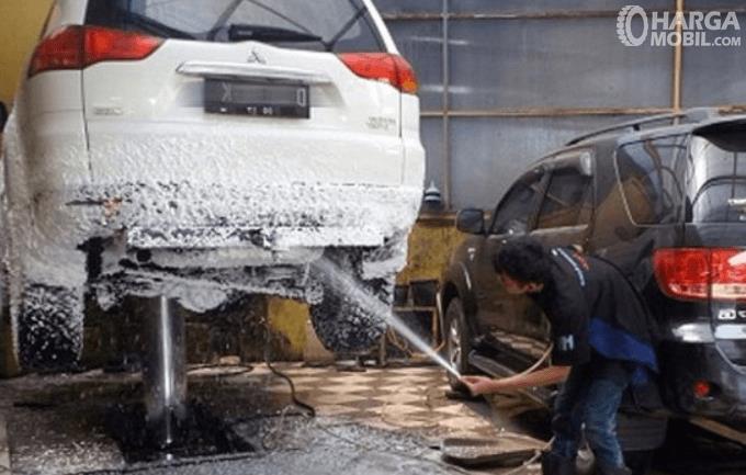 Gambar ini menunjukkan seseorang mencuci kolong mobil warna putih